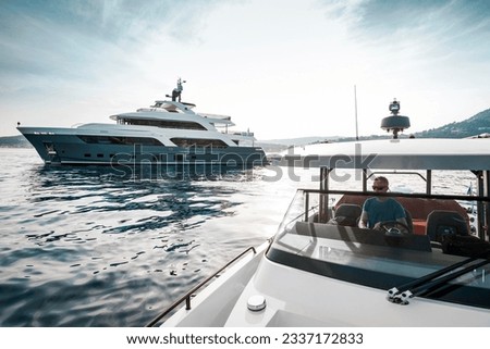Superyacht deckhand crew on duty, driving chase boat tender next to a 38 meter modern superyacht at anchor in the Bay of Saint-Jean-Cap-Ferrat, south of France Royalty-Free Stock Photo #2337172833