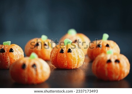 Halloween cute pumpkin orange fruit with chocolate eyes. Healthy dessert snack with funny faces for child's party decoration. Selective focus on center with blurred foreground and background. 