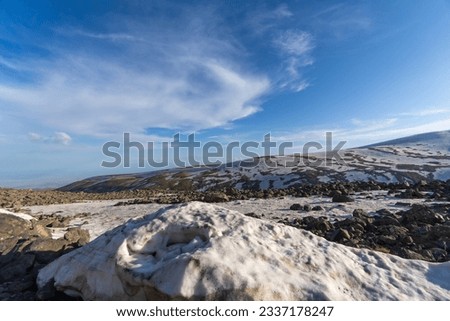 View of snow-capped mountains in summer on a sunny bright day with blue sky and clouds. Beautiful incredible mountain landscape with paved road, green grass and snow