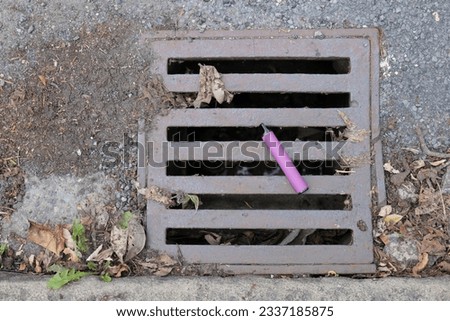 A purple e-cigarette vape has been discarded and left lying on a metal water drain cover. Royalty-Free Stock Photo #2337185875
