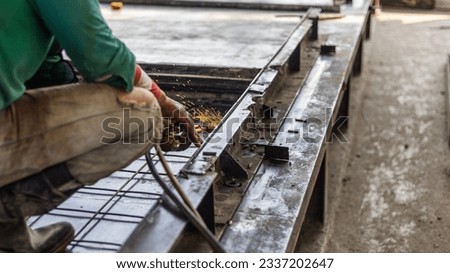 Worker with safety hat is welding pieces of metal mold together for precast floor production. Technician is preparing a block for concrete floor making.
