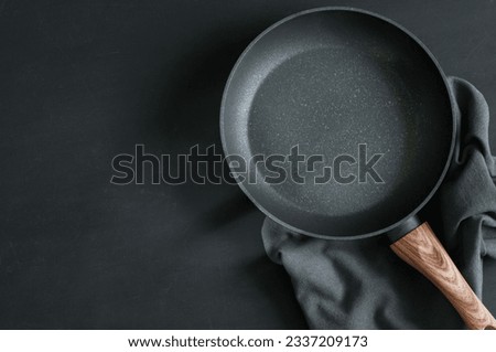 Empty frying pan and napkin on black background, top view with copy space for text