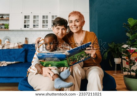 Mature lesbian couple reading book with their adopted child at home Royalty-Free Stock Photo #2337211021