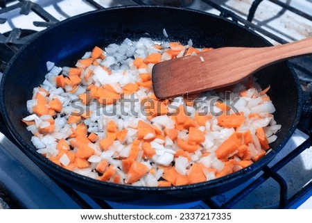 Carrots and onions are fried in a pan and mixed with a wooden spatula Royalty-Free Stock Photo #2337217335