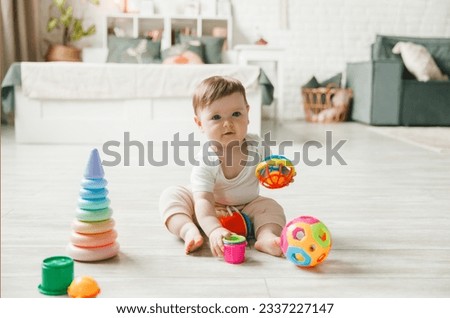 baby 6-9 months old playing with a colorful rainbow toy pyramid sitting in a white sunny bedroom. Toys for small children. Children's interior. A child with an educational toy. Royalty-Free Stock Photo #2337227147
