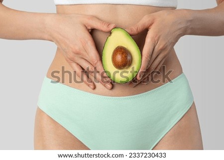 Avocado in female hands on the background of the body. Women's health, fertility, diet. Royalty-Free Stock Photo #2337230433