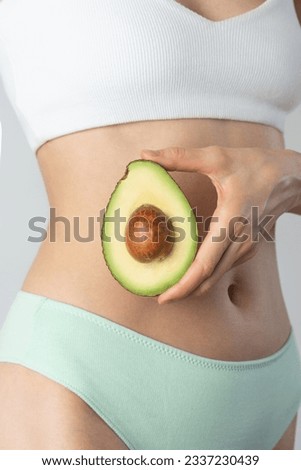 Avocado in female hands on the background of the body. Women's health, fertility, diet.