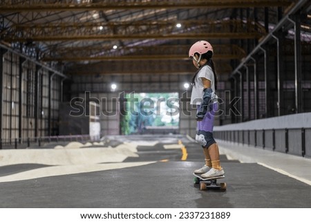 asian child skater or kid girl start playing skateboard and fun ride surf skate at indoor pump track skate park by extreme sports surfing to wearing helmet elbow pads wrist knee guard for body safety Royalty-Free Stock Photo #2337231889