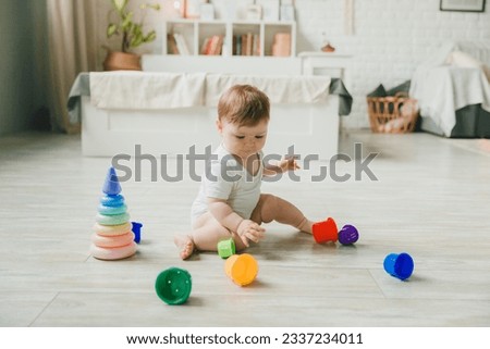 baby 6-9 months old playing with a colorful rainbow toy pyramid sitting in a white sunny bedroom. Toys for small children. Children's interior. A child with an educational toy. Royalty-Free Stock Photo #2337234011