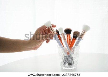 Woman’s hand pick up a professional makeup brushes set in glass on table. Still life photo makeup artist tools.