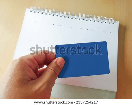 Hand holding the blue credit card and checking due date of payment on the white calendar. Make a