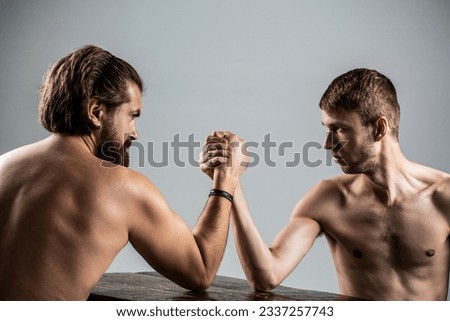 Arms wrestling thin hand, big strong arm in studio. Two man's hands clasped arm wrestling, strong and weak, unequal match. Arm wrestling. Heavily muscled bearded man arm wrestling a puny weak man.