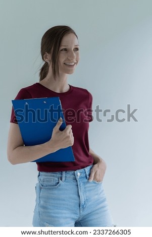 Attractive young office worker holding a  binder as she looks at the camera with a sweet friendly smile