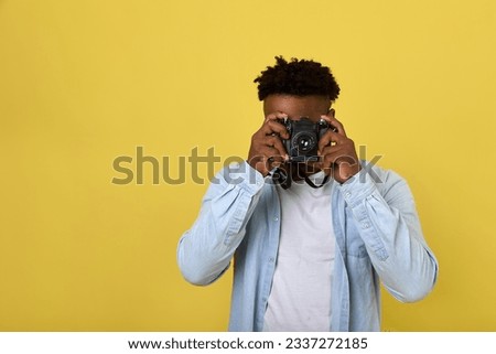Professional black photographer in a long-sleeved shirt looks into the camera lens. A popular modern photojournalist takes pictures in a yellow studio