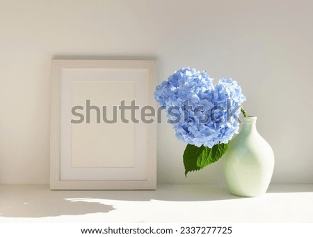 Frame mockup, ceramic vase with Blue hydrangea flowers on table near white wall. Photo frame, poster template . Copy space.
