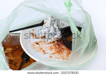 Dirty, used disposable tableware in a plastic bag. Foil, plastic plates and forks on a white background. Used plastic dishes are dirty after eating. Home delivery Mexican food. 