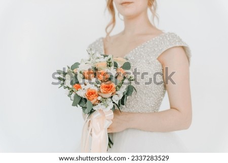 wedding bouquet in bride hands, young caucasian woman in white dress, white and red roses bouquet with cream ribbons, white background