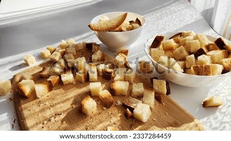Homemade slices of diced dry white rye bread on cutting board and white plate. Crackers for food, healthy eating on table in sunny day. Top view Royalty-Free Stock Photo #2337284459