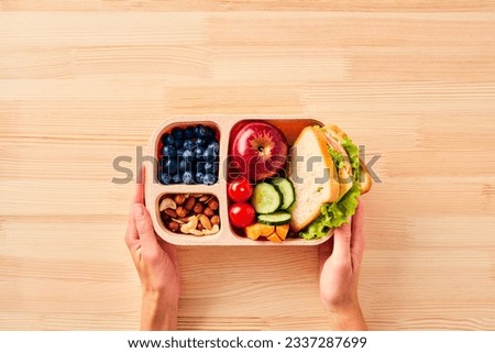 Women's hands hold lunchbox of healthy food over wooden table.