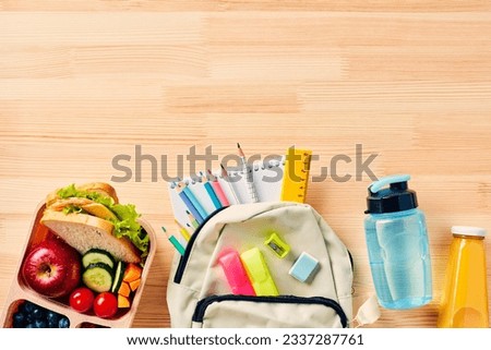 School backpack with supplies, bottles of water and juice, lunch box with healthy food on wooden background. Flat lay, top view.