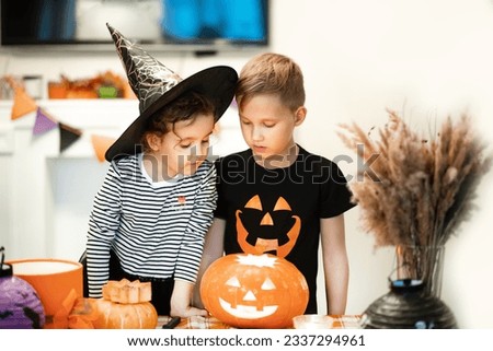 Young kid boy carving traditional Halloween jack-o-lanterns with scary face for party at home