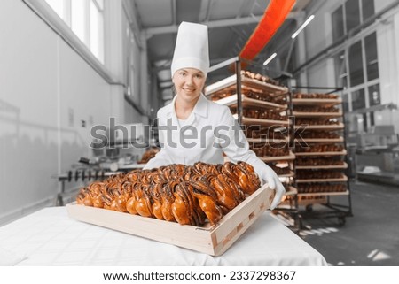Happy worker woman baker in chef uniform hold freshly bakery poppy seed bun bread. industrial factory food production.