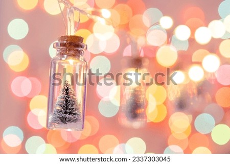 Merry Christmas and happy new year. Hanging small Christmas tree in glass jar on pine branches Christmas tree garland and ornaments over abstract bokeh