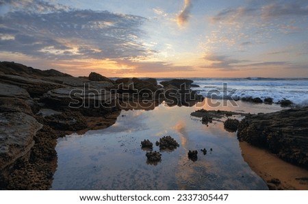 Early morning skies, ocean waves and incoming tidal flows over sea squirts. Bungan Beach, Australia