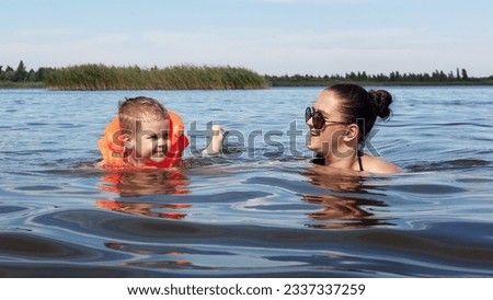 Hot summer day, little boy in orange inflatable vest swimming in the lake with his mother.