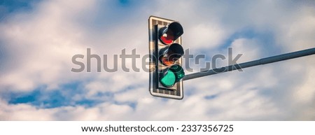 A traffic light with a green light on a background of a blue sky with white clouds. Banner