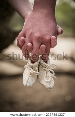 Parents holding hands and small baby woollen socks. Focus on the small shoes. Parents expecting a child. Maternity leave, parental leave. Love photoshoot Royalty-Free Stock Photo #2337361337