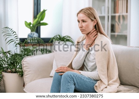 Woman coughs and feels pain in her throat. Sick upset female having painful sensations, sitting on sofa at home covered warmth wool blanket. Concept of feeling bad, health problem, illness Royalty-Free Stock Photo #2337380275