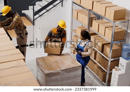 African american warehouse loader giving cardboard box to supervisor in post office storage room. Industrial storehouse woman manager inspecting freight packaging top view Royalty-Free Stock Photo #2337381999