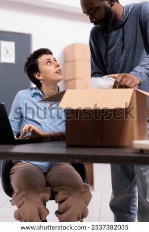 Storehouse employees preparing customers packages putting order in cardboard box wrapped with bubble wrap while discussing shipping detalies, Diverse team working in delivery department in warehouse