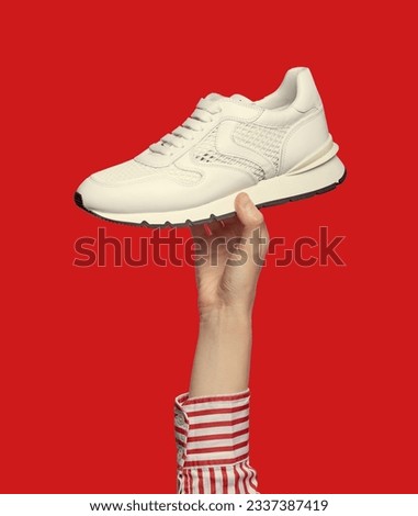A woman's hand holding a modern white sneaker, isolated on a red background. Sport and active lifestyle.  Outlet marketing poster. Summer shoe sale campaign