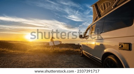Surfergirl sitting near her mini van and looking on the ocean at summer sunset  with a surfboard on her side Royalty-Free Stock Photo #2337391717