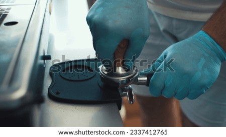 Gloved hands pressing coffee into stainless steel filter Royalty-Free Stock Photo #2337412765