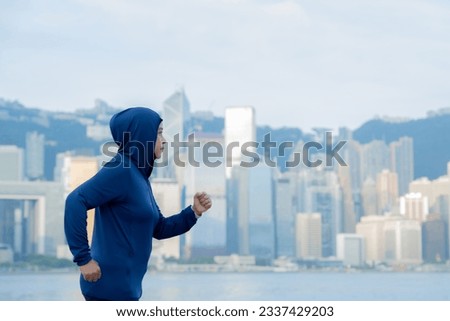 Glad smiling young asian muslim woman in hijab with fitness tracker running on building background outdoor. Fitness outside, jogging in morning, body and health care, training, concept muslim sport.