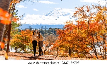 Happy Asian woman travel Japan on holiday vacation. Attractive girl friends using mobile phone taking selfie together while travel Mt.Fuji and looking beautiful red maple tree leaf falling in autumn Royalty-Free Stock Photo #2337439793