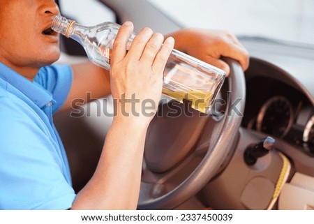 Close up man holds bottle of whiskey to drink in car. Concept , Stop driving while drinking alcohol or whiskey campaign. Illegal and dangerous to drive vehicle that leads to accident. Royalty-Free Stock Photo #2337450039