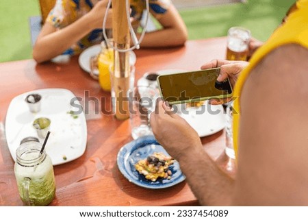 unrecognizable members of the lgbt community enjoying snacks and drinks at an outdoor restaurant and taking cell phone pictures of the food. High quality photo