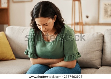 Stress, stomach pain and woman on a sofa with menstruation, gas or constipation, pms or nausea at home. Gut health, anxiety and lady with tummy ache in living room from ibs, bloated or endometriosis Royalty-Free Stock Photo #2337463923