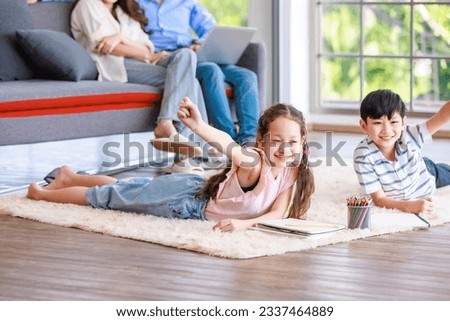 Closeup Asian happy cheerful joyful family little boy son and girl daughter laydown on carpet floor helping teaching painting drawing cartoon with color pencils in living room.