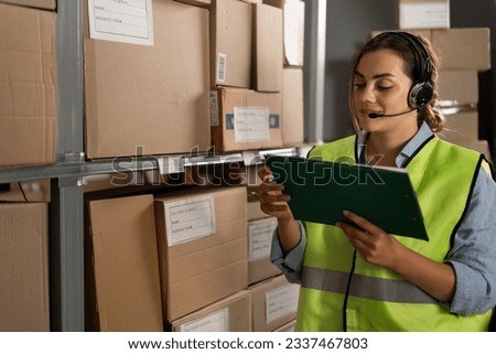A warehouse worker checks the items against an inventory list on a clipboard. A logistics manager takes inventory using a warehouse management system in a distribution center.