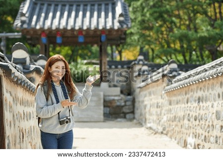 A young woman wearing a camera and taking pictures while traveling to tourist attractions with traditional Korean houses