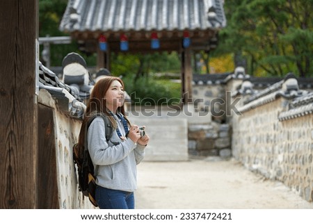 A young woman wearing a camera and taking pictures while traveling to tourist attractions with traditional Korean houses