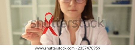 Infectious disease doctor holding red ribbon in his hands on hiv day closeup. Prevention and treatment of AIDS concept