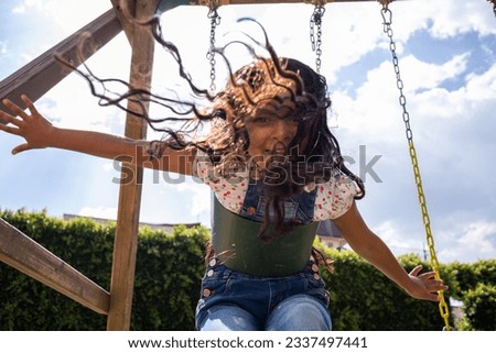child girl at the playground playing on a swing, hispanic kid smiling and having fun at the park, low angle shot