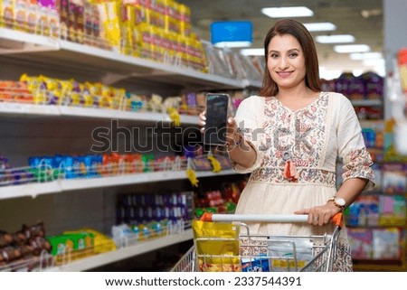 Indian woman showing smartphone screen at grocery shop. Royalty-Free Stock Photo #2337544391