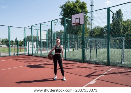 Young sports girl with a basketball on the basketball court outdoors, active weekend.